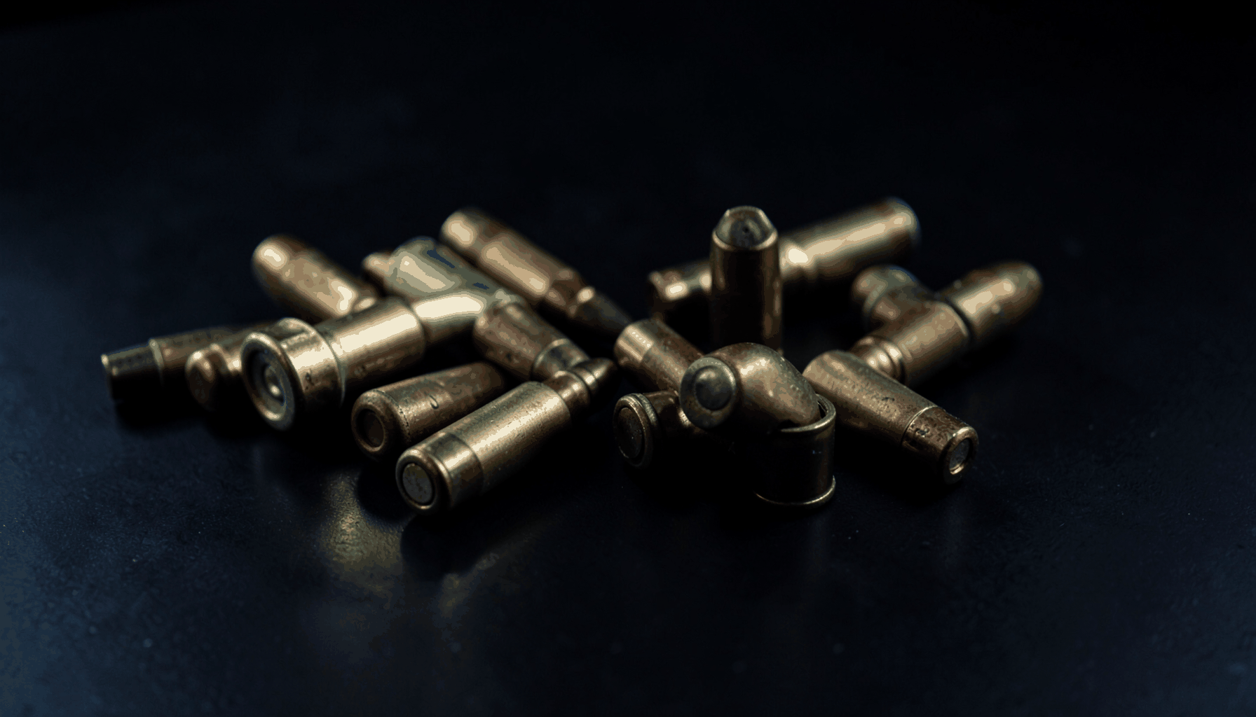 Dark atmospheric image of ammunition rounds arranged on a matte black surface with subtle blue-gray reflections